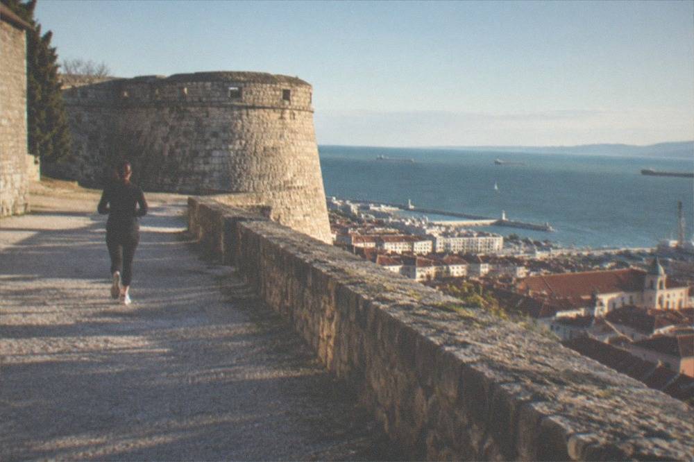 A stone castle wall and round bastion overlooking red rooftops and the Adriatic sea in Trieste