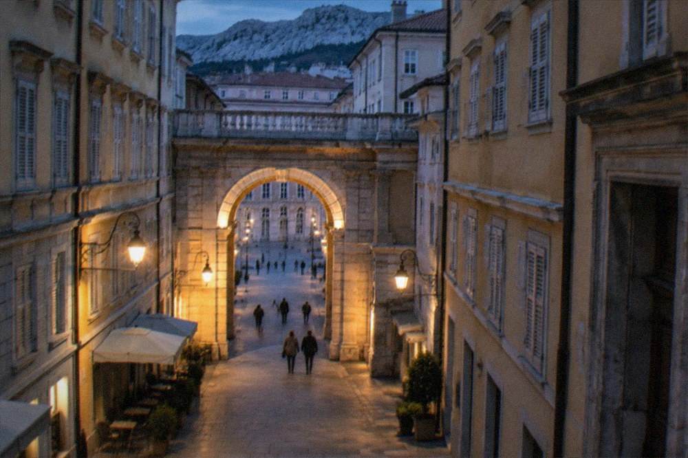 Evening view of a lit stone arch in a quiet Trieste old-town lane