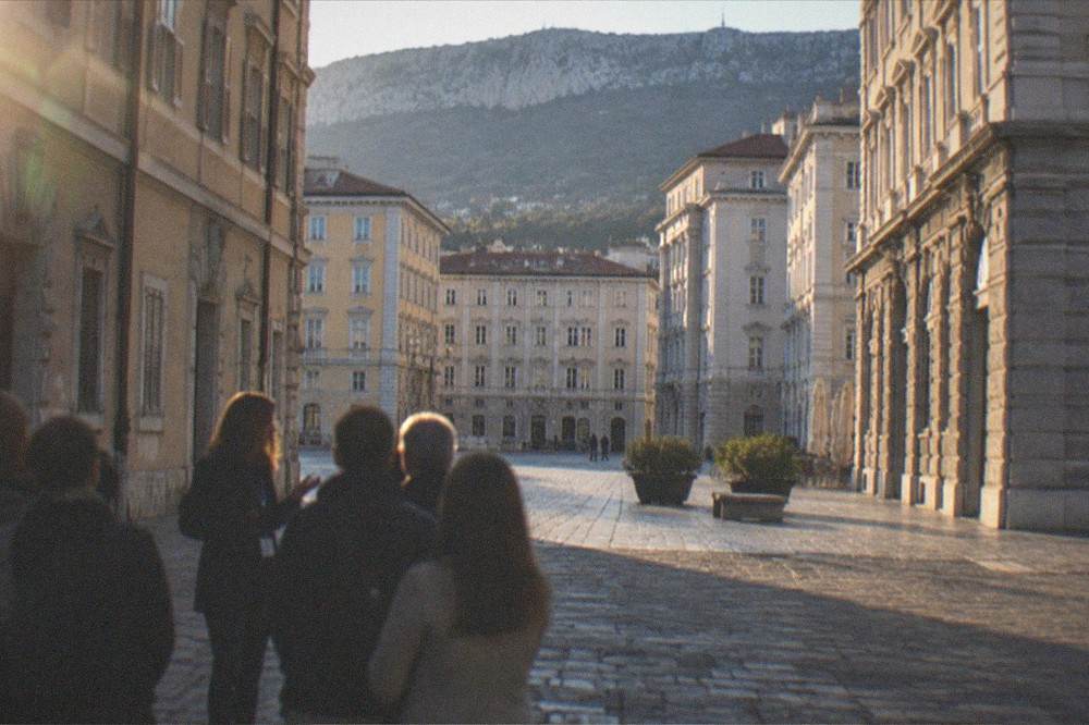 A local guide talking with a small group of visitors on a cobbled square in Trieste