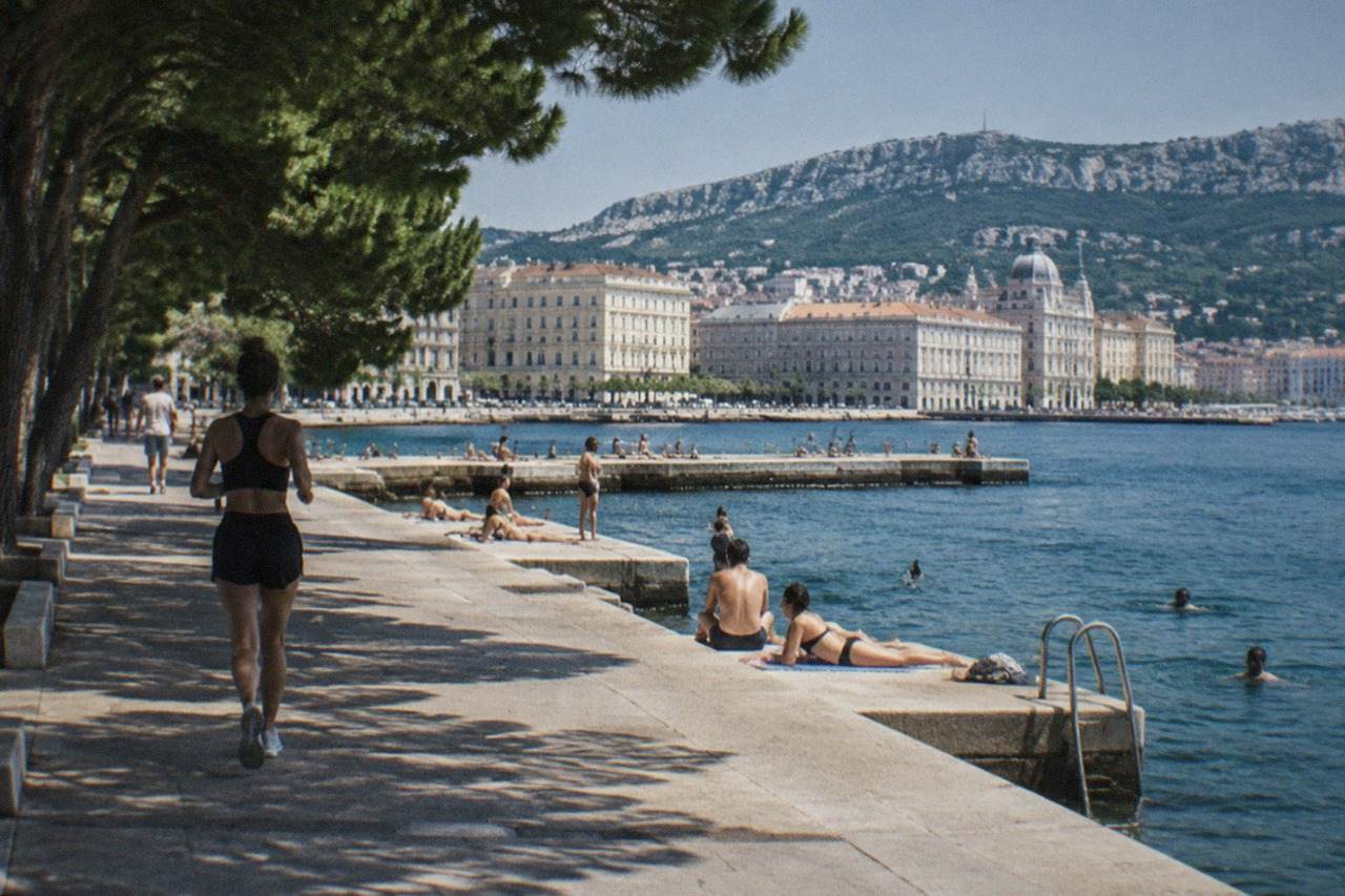 Swimmers and sunbathers on concrete platforms beside the sea at a historic bathing establishment on the Trieste waterfront