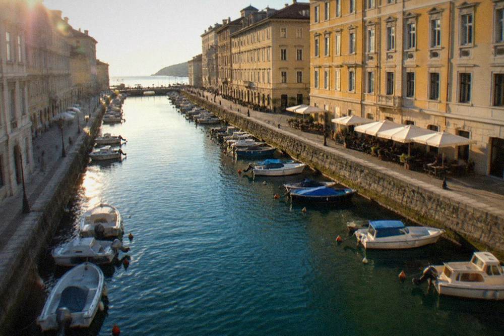 Small boats moored along the quay of a city canal with café tables on the bank