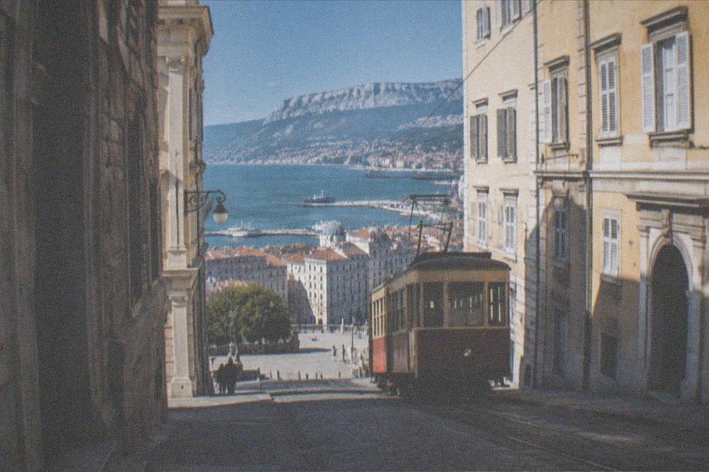 A vintage tram climbing a hill above Trieste with the sea and city rooftops below