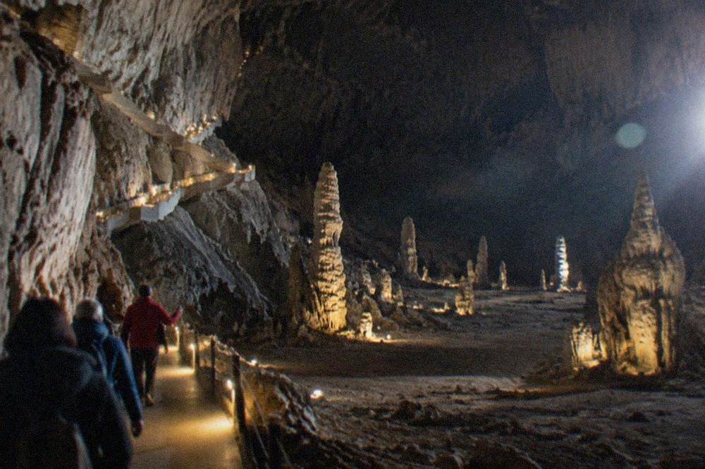 A guide leading a small group of visitors along a lamp-lit walkway inside a large limestone cave