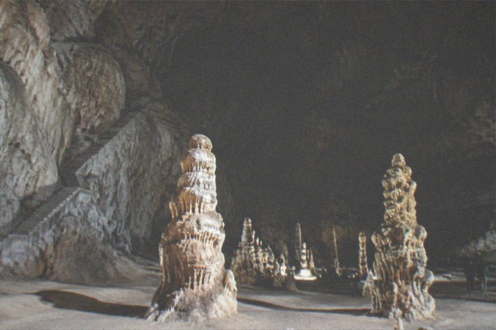 Stalagmites and flowstone formations lit inside a large limestone chamber of a show cave