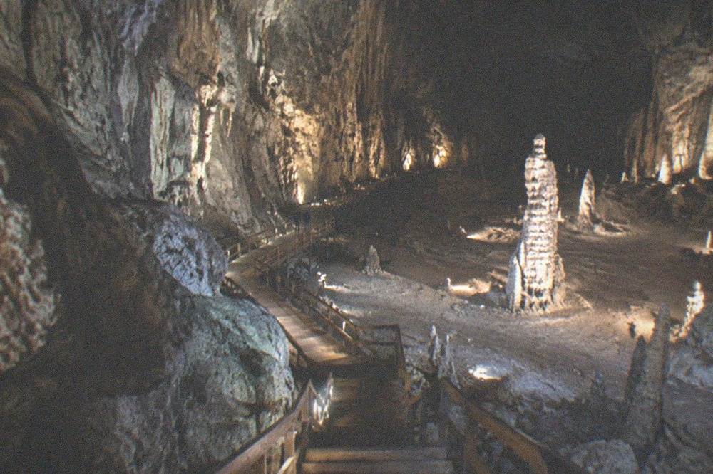 A wooden staircase and walkway descending between rock walls inside a large illuminated cave chamber