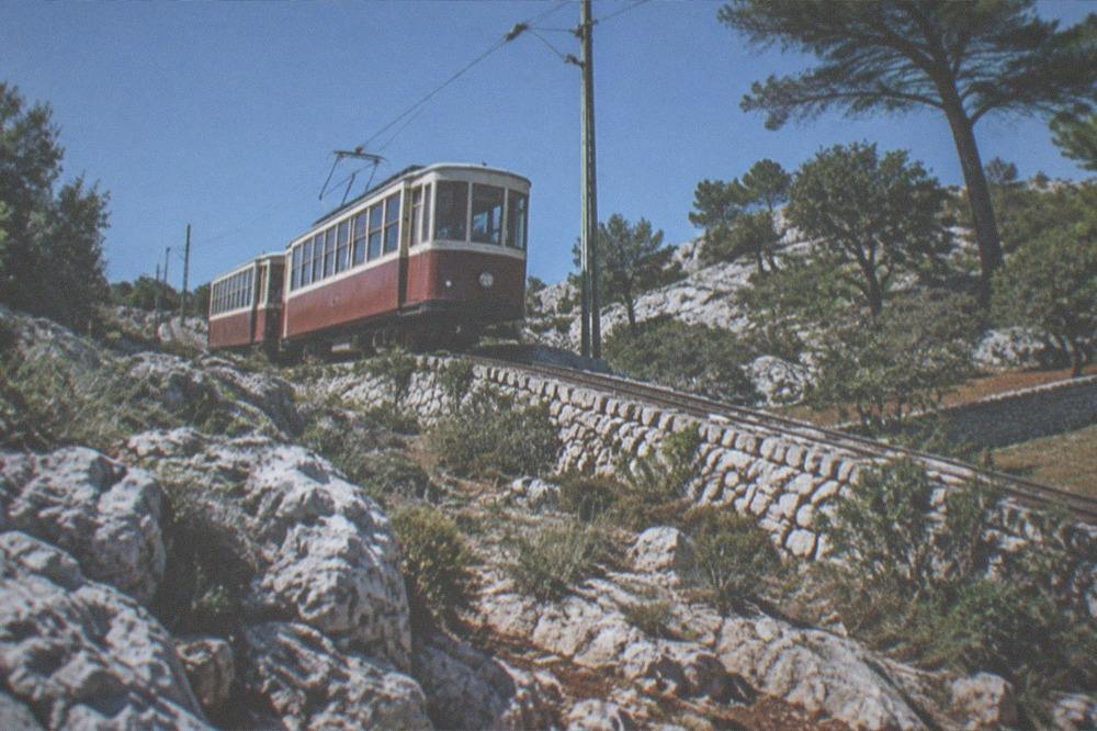 A vintage two-carriage tram climbing a steep street on the karst slope above Trieste