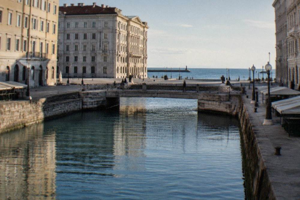 A wide seaside square with grand ornate buildings on three sides and open sea on the fourth