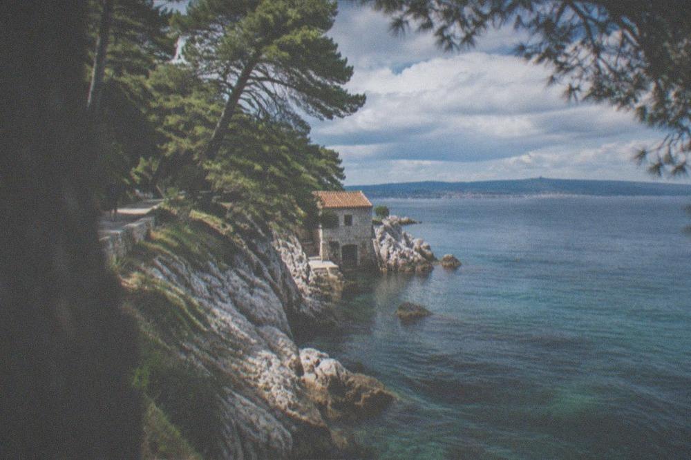 A coastal footpath with pine trees and the blue gulf stretching toward distant hills