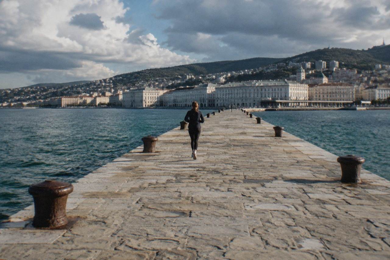 A stone pier reaching into a calm Adriatic gulf with a city skyline behind it