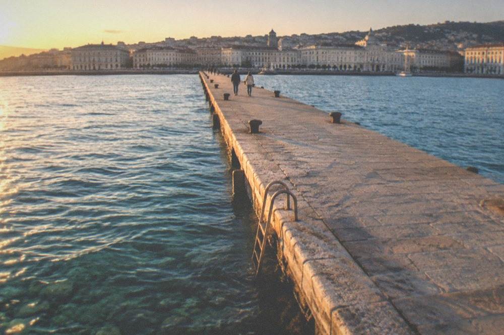 Clear shallow water over stones beside a stone pier with a ladder into the sea