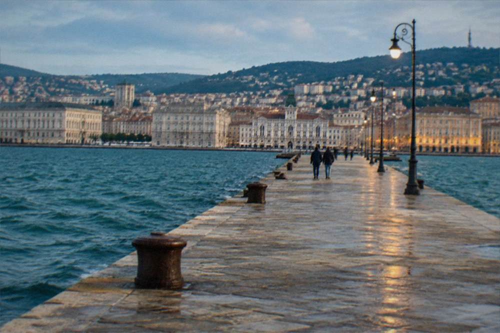 A stone pier at night lit by warm lamps with a lit square behind it