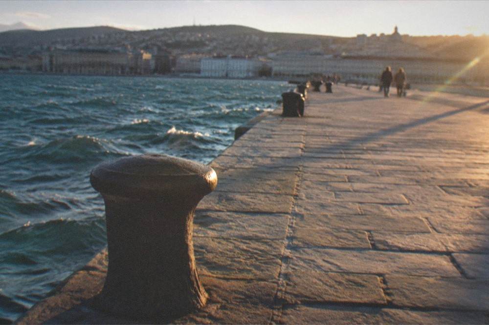 A bare stone walkway over open sea with wind ruffling the water surface