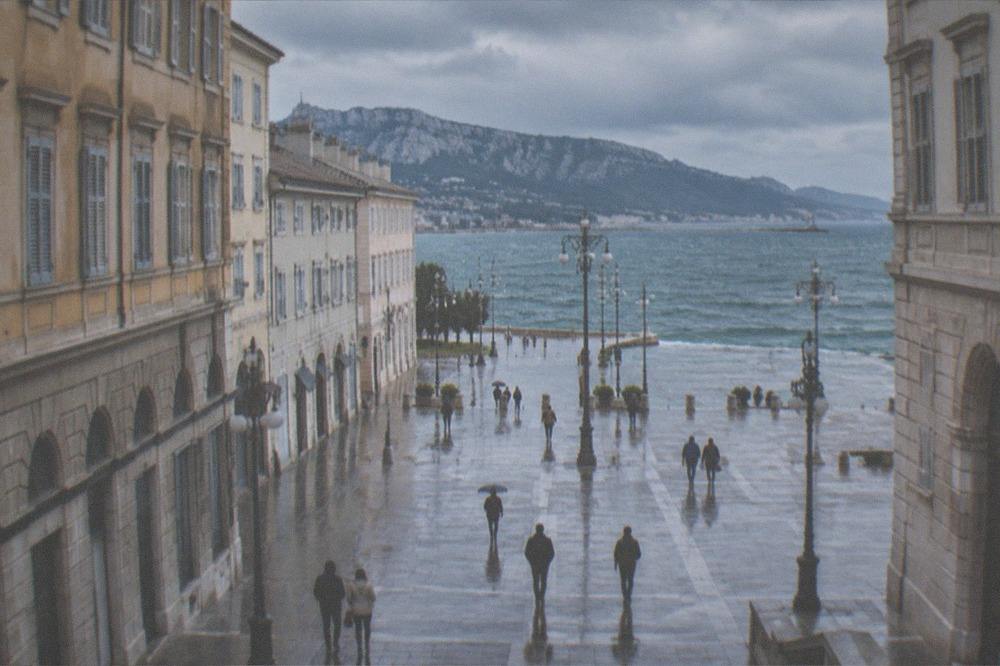 The Trieste seafront under a cloudy November sky with wet paving and the sea beyond