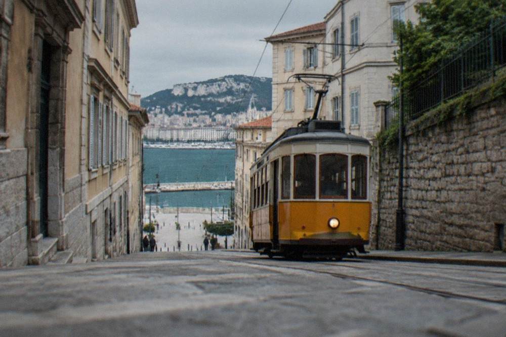 The tram climbing a steep street with stone walls and a view of the sea below