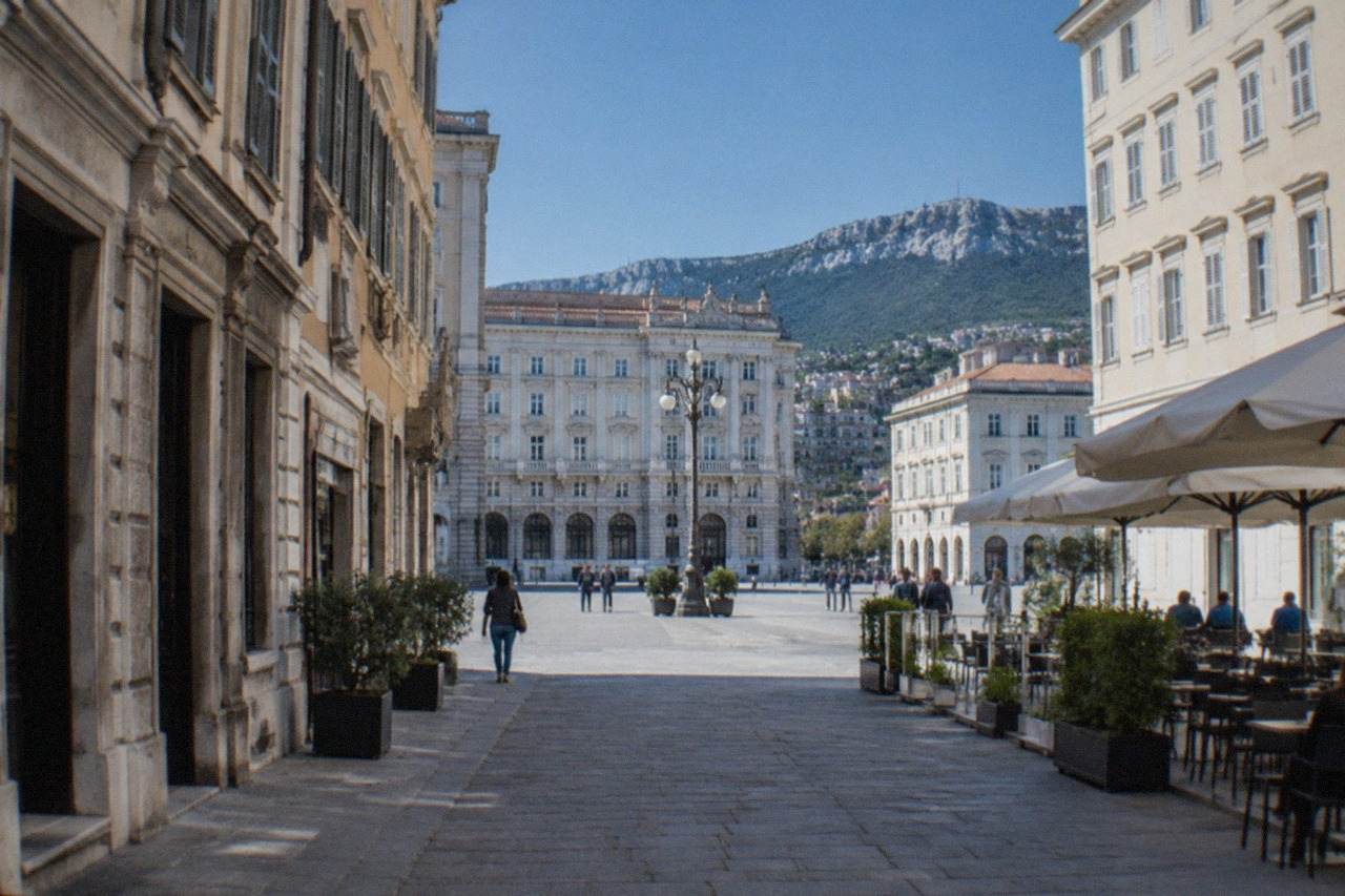 An elegant square in Trieste lined with neoclassical buildings and outdoor cafe tables