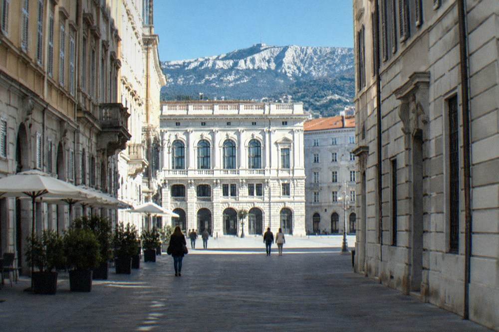 A neoclassical palace facade with tall arched windows on a square in central Trieste