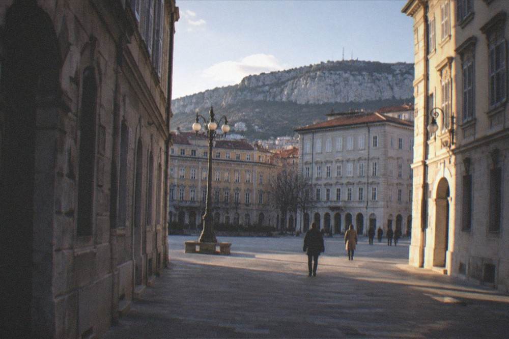 Evening light on the facades around a quiet square in Trieste with a few people strolling
