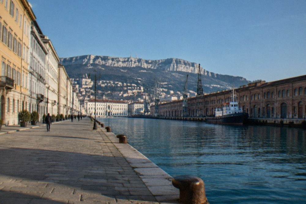 Rows of large brick port warehouses along a straight quay in Trieste
