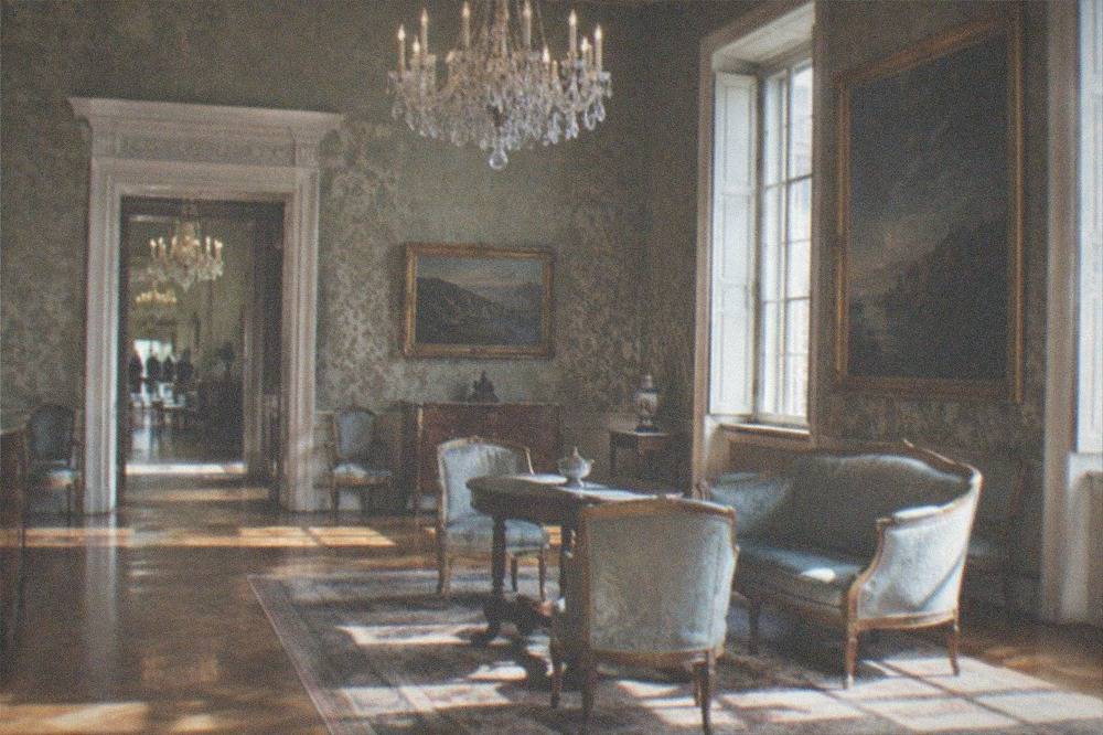 An ornate drawing room with period furniture, chandeliers and framed paintings on patterned walls