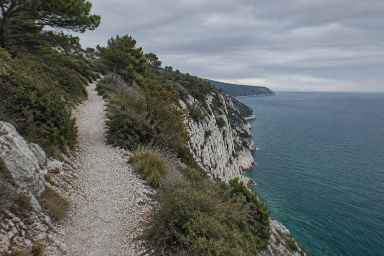 A narrow stone path running along a white limestone cliff above the blue Adriatic Sea