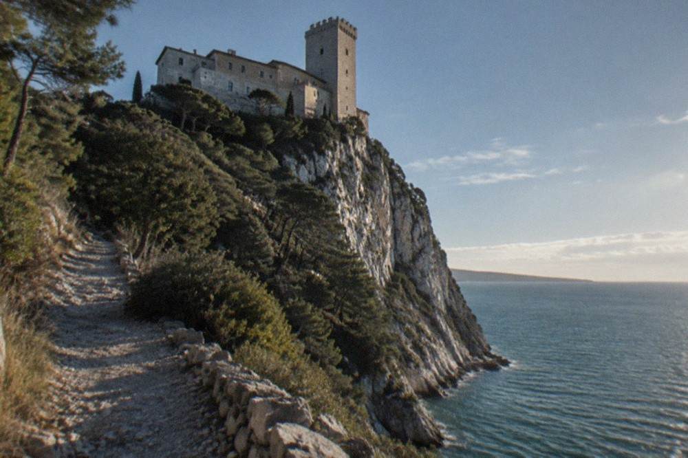 Duino Castle seen from a coastal path with the sea behind it