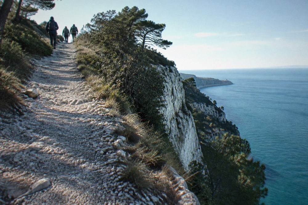 Walkers on a gravel clifftop path with the Adriatic Sea far below