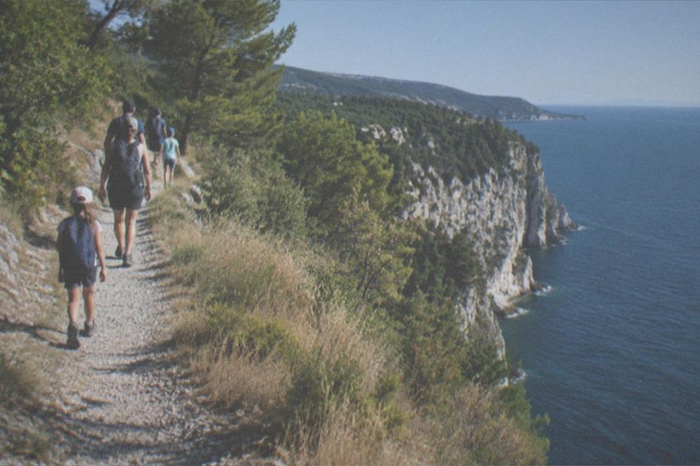 A family walking a coastal footpath with the sea on one side and dry grassland on the other