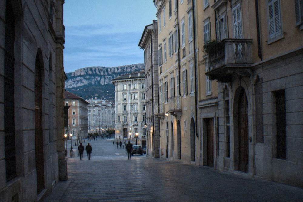 An urban street in Trieste with apartment buildings leading toward the southern industrial quarters