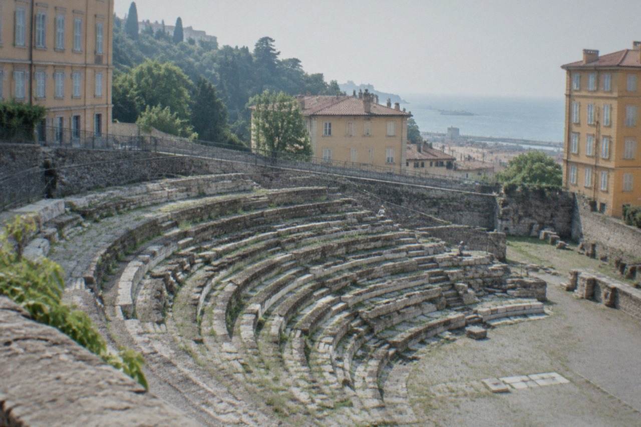 Ancient Roman theatre seats rising at the foot of a wooded hill in Trieste, Italy, with old town buildings behind