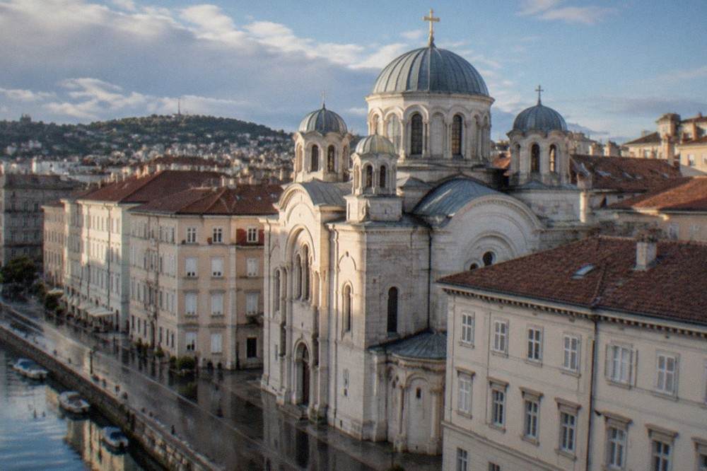 Sunlight falling on the upper facade and cross of the Saint Spyridon church above old-town rooftops