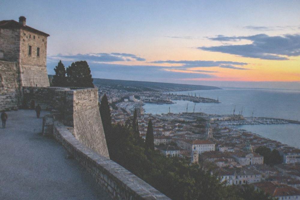 The ramparts of San Giusto Castle overlooking Trieste rooftops and the sea at golden hour