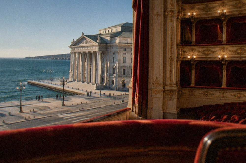 A gilded opera house auditorium with red velvet seats seen from the balcony