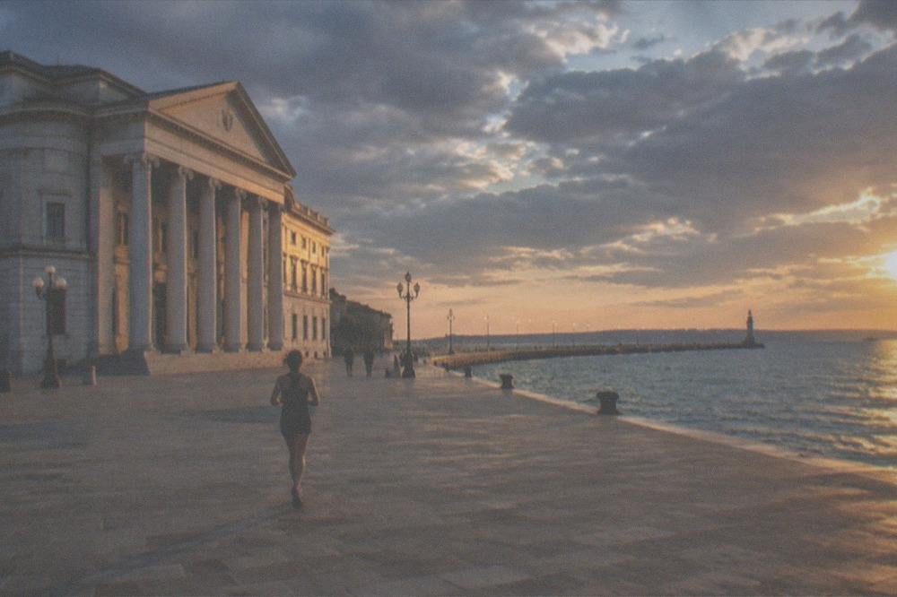 A wide seafront square lit by golden hour with a lit pier stretching into calm water