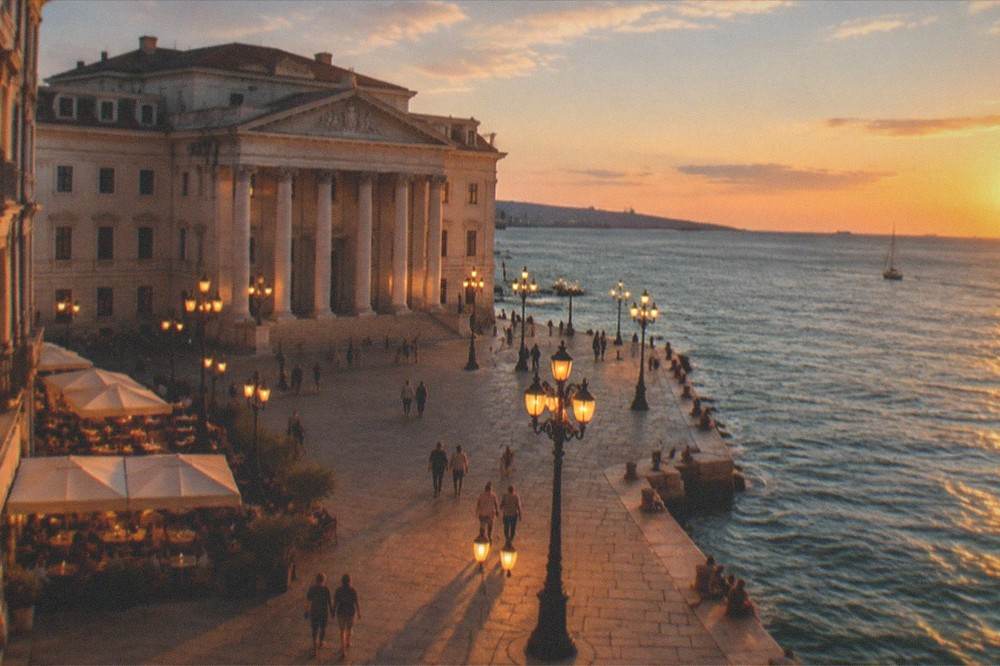 A lamplit Italian square at night with cafe tables and people strolling