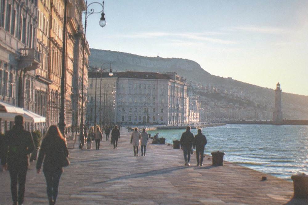 People strolling the Trieste seafront with the lighthouse in the distance