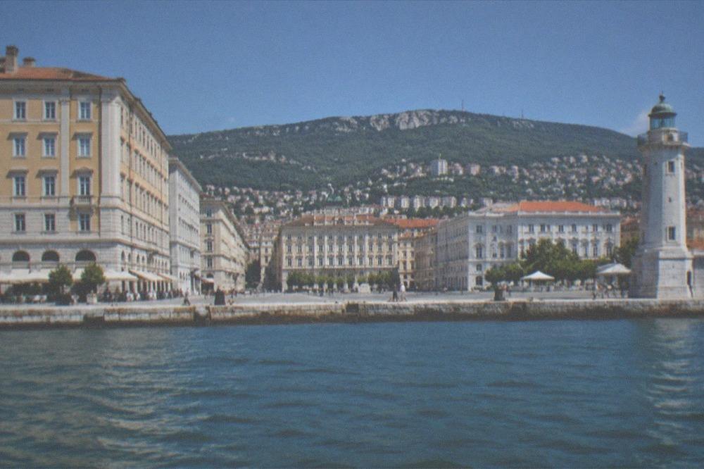 The Trieste waterfront seen from the water with the lighthouse and the hills behind the city