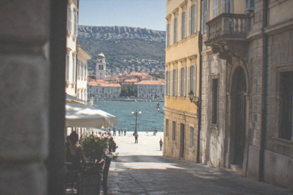 Terracotta rooftops of a small Adriatic coastal town with a bell tower and the sea beyond