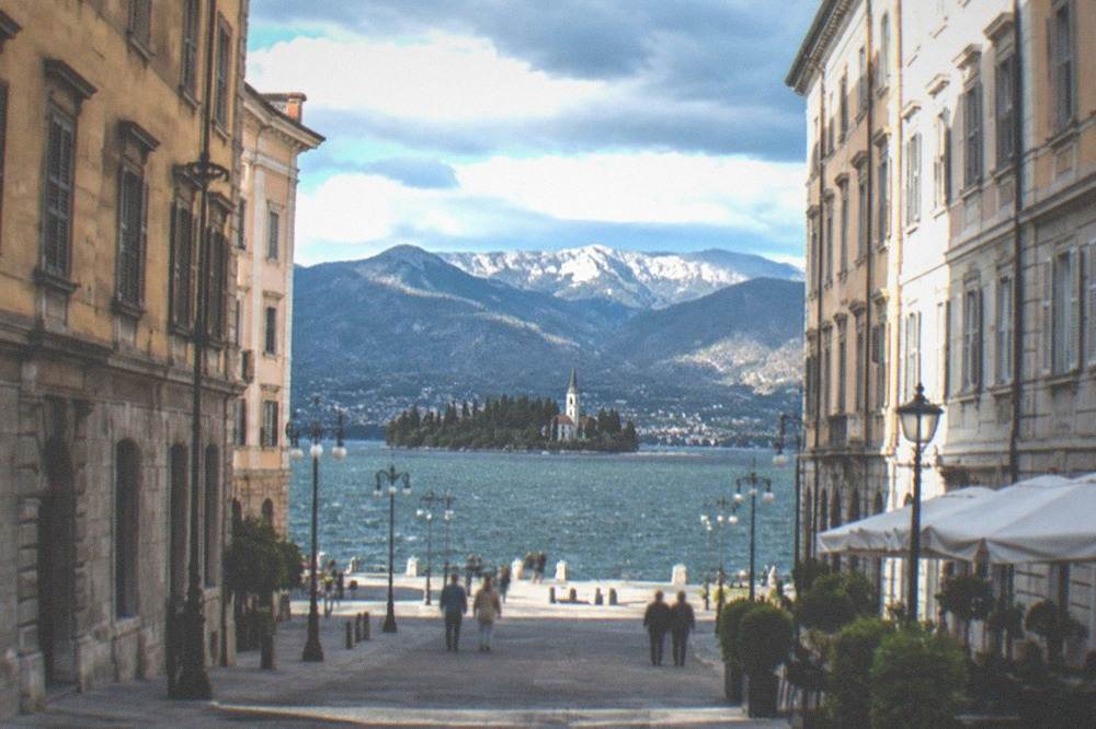A lake with a small wooded island and a church steeple, mountains rising behind it