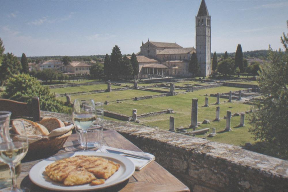 A simple trattoria table set with bread, glasses of white wine and a plate of frico