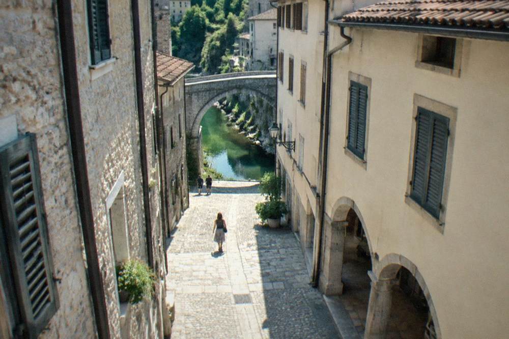 A narrow medieval street with stone buildings and shuttered windows in a Friuli hill town