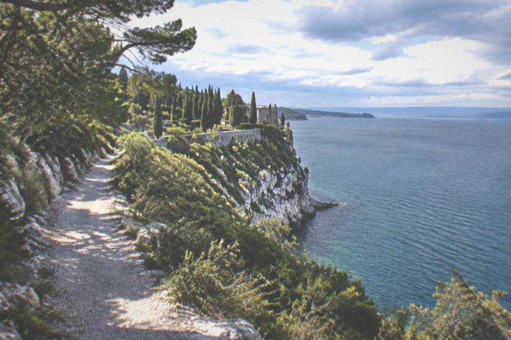 A terraced castle garden above the sea with cypress trees and a view along the coast