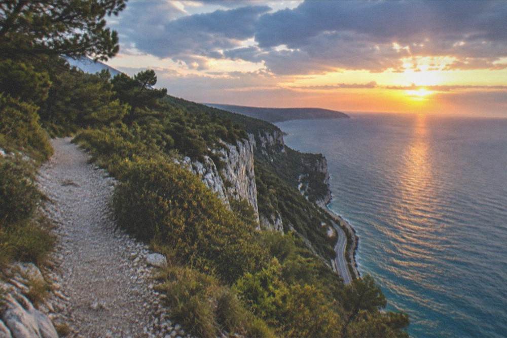A sunset over the Adriatic seen from a cliff top with the coast road below
