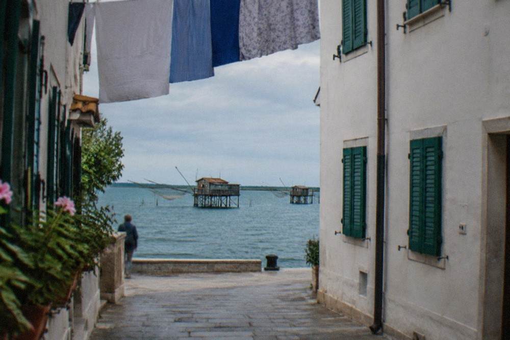A narrow lane in a small island old town with white walls, green shutters and laundry overhead