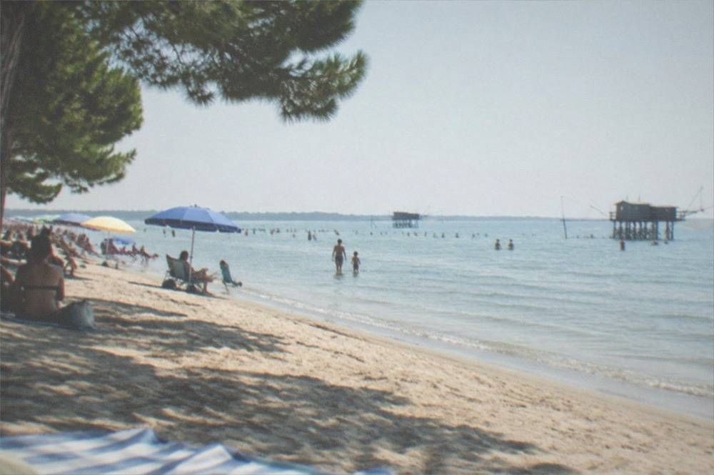 A wide sandy beach with sun umbrellas and calm shallow water on a summer day
