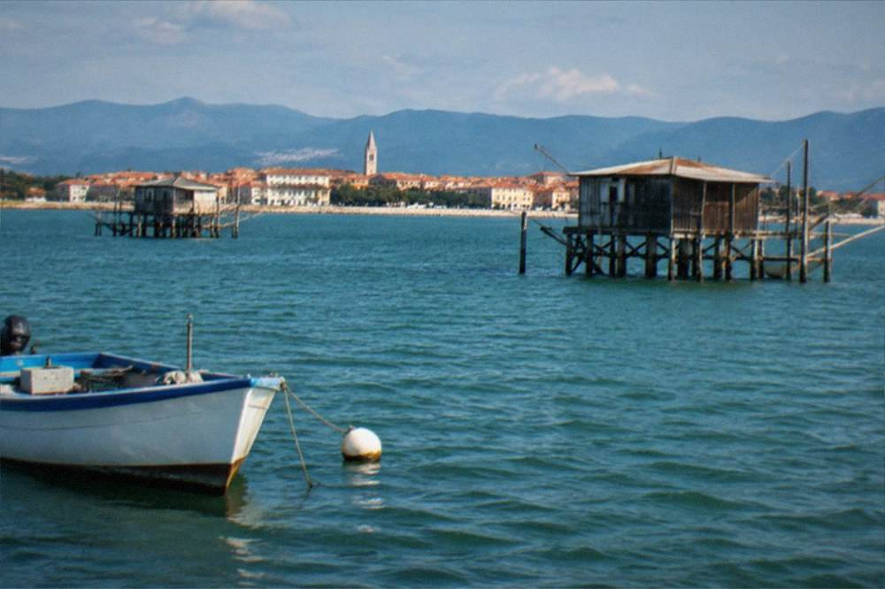 A small coastal town of terracotta rooftops seen from the water with hills behind