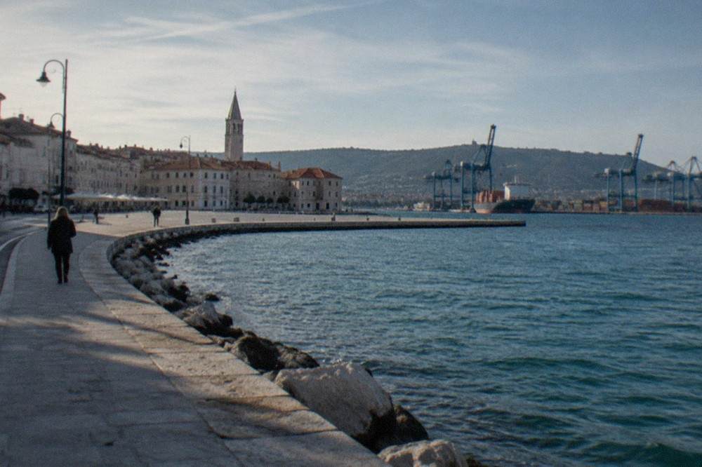 A coastal road curving along a shoreline with hills behind it