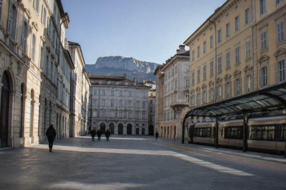 A train waiting at a Trieste station platform under a curved glazed roof