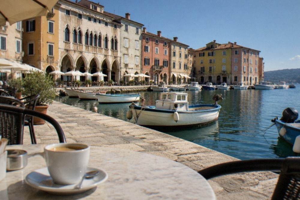 An arcaded seaside piazza with cafe tables and old painted facades