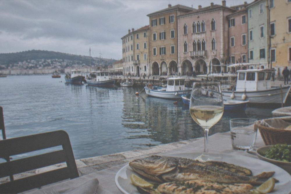 A table of grilled Adriatic fish and white wine beside a harbour