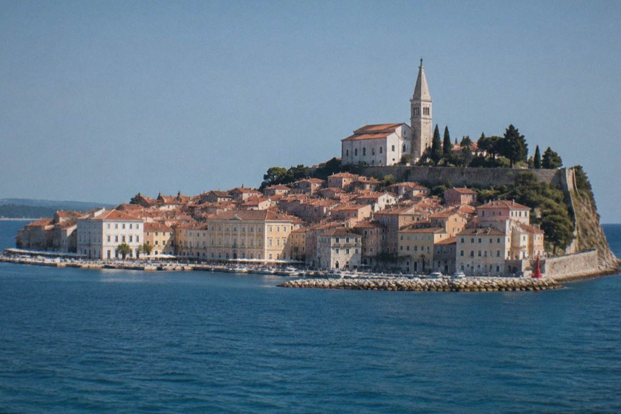 The old town of Piran on a peninsula seen from the water, with terracotta roofs and a bell tower above the harbour.